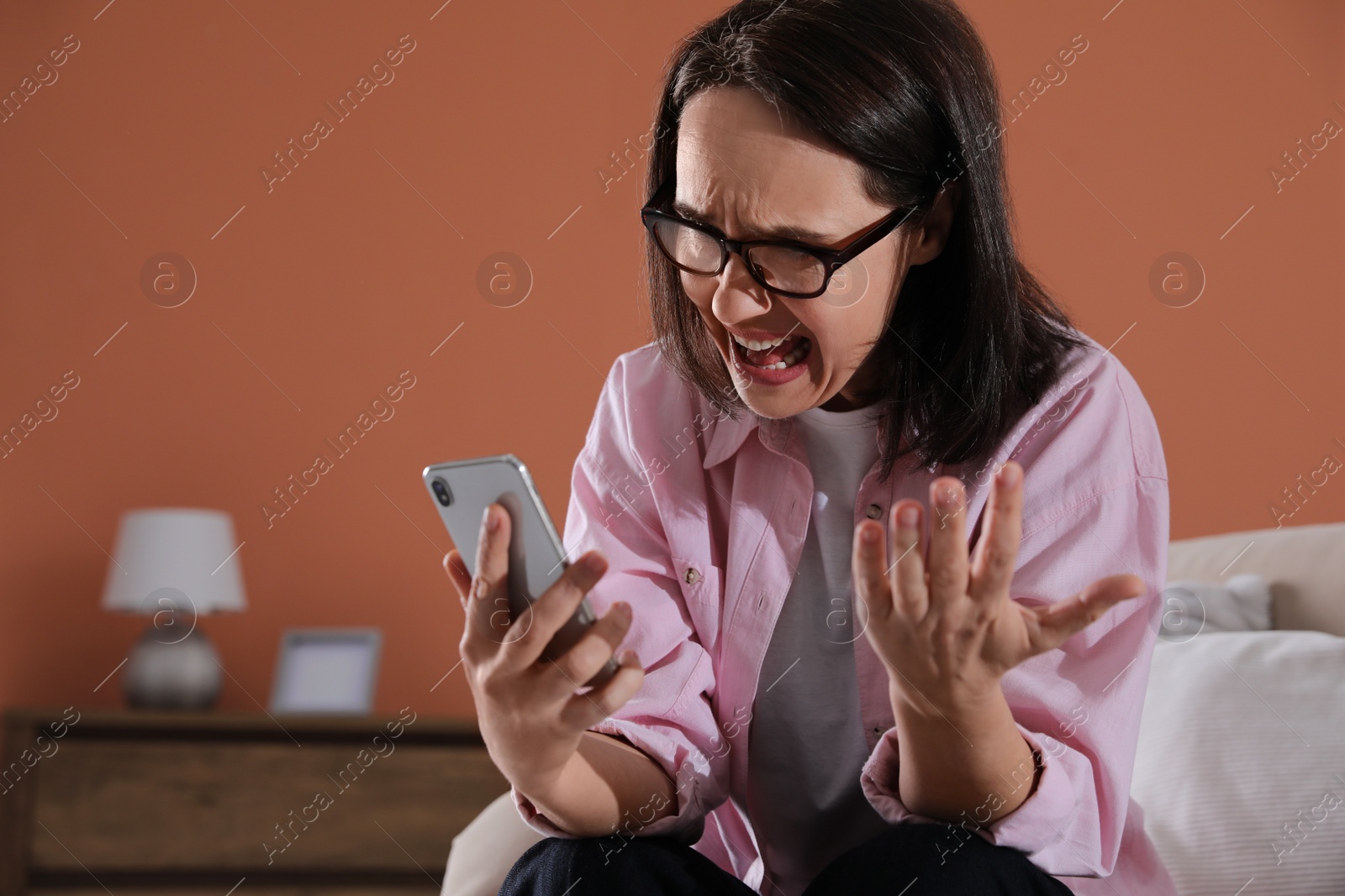 Photo of Emotional woman with smartphone at home. Online hate concept