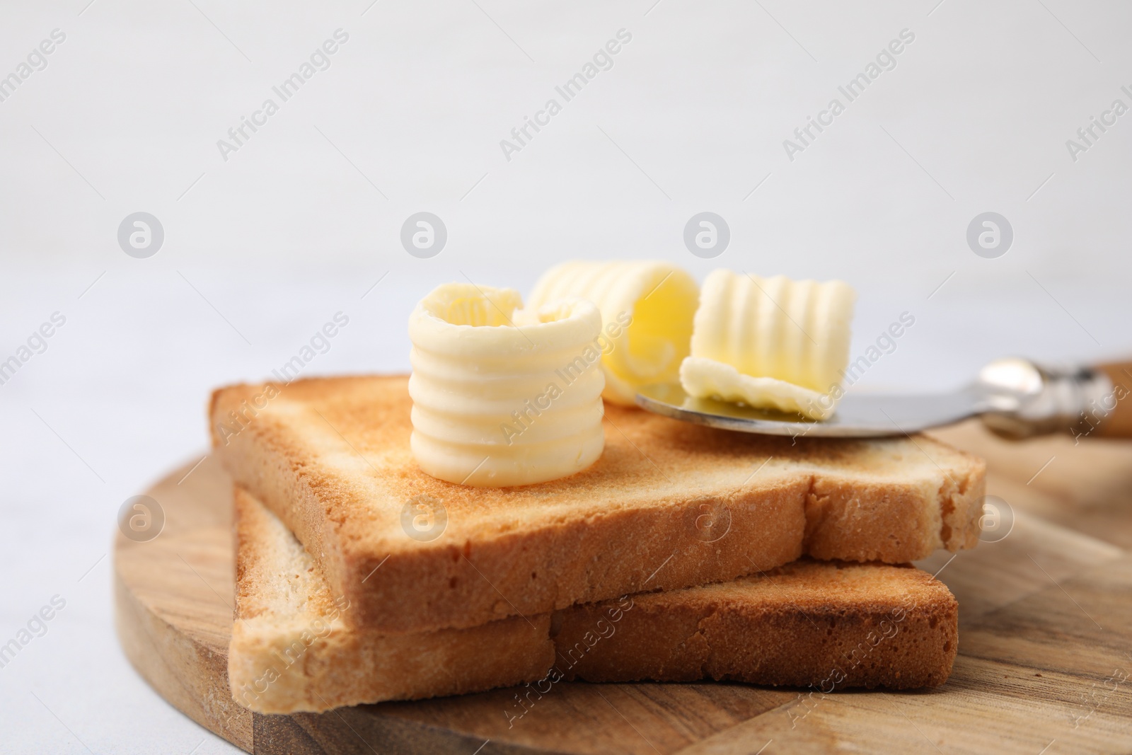 Photo of Tasty butter curls, knife and toasts on white table, closeup