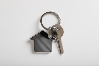 Key with trinket in shape of house on white background, top view. Real estate agent services