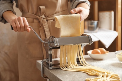 Photo of Young woman preparing noodles with pasta maker at table