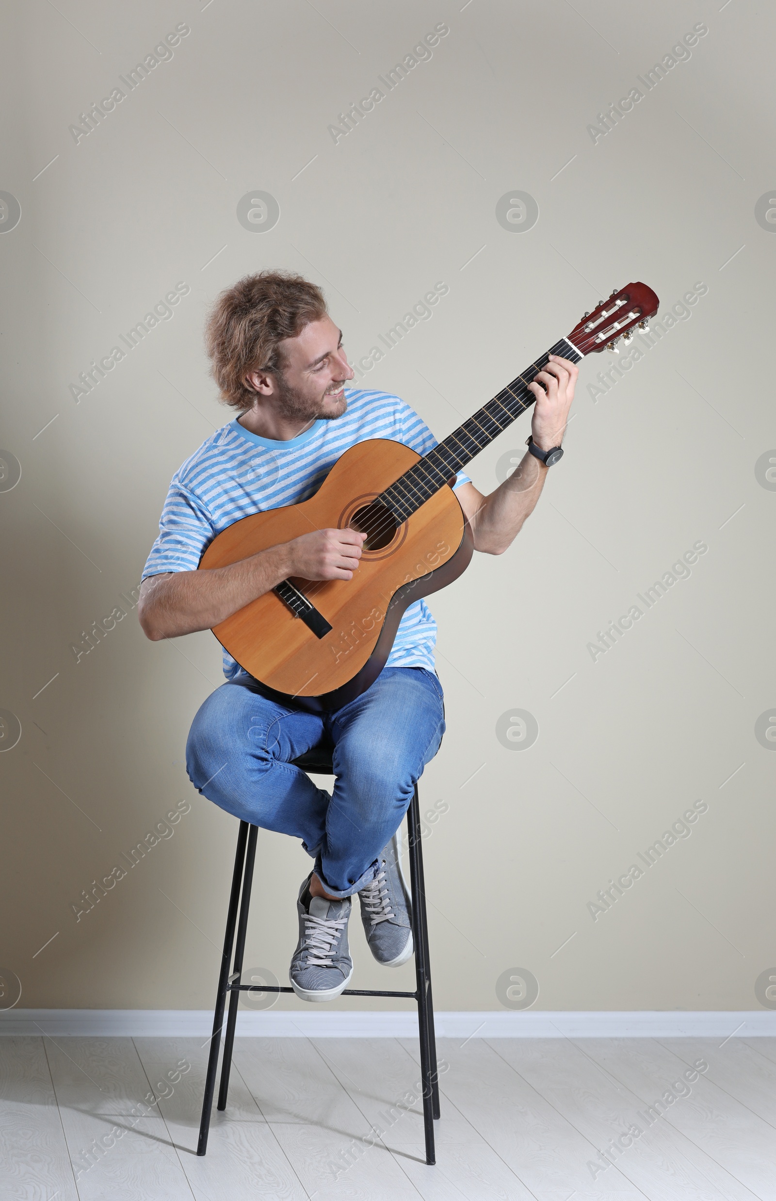 Photo of Young man playing acoustic guitar near grey wall