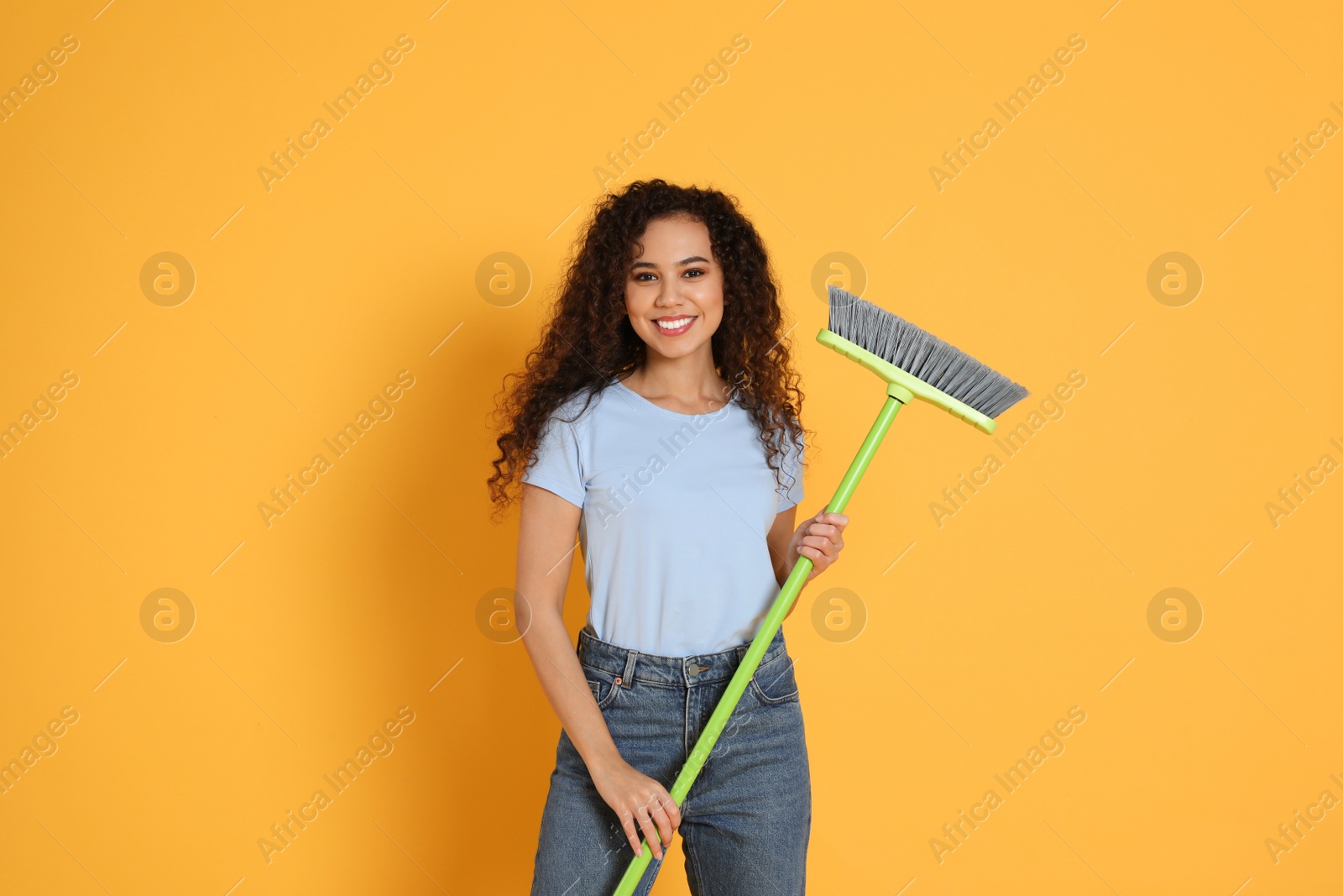 Photo of African American woman with green broom on orange background