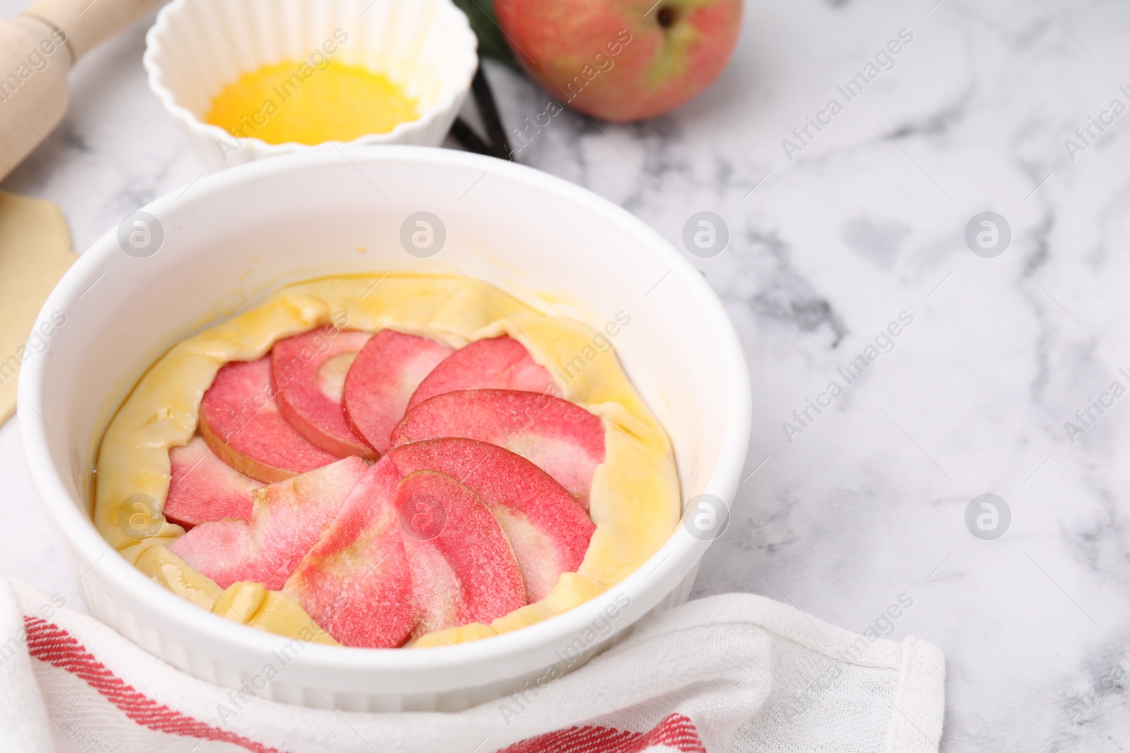 Photo of Baking dish with fresh dough and apples on white marble table, closeup with space for text. Making galette