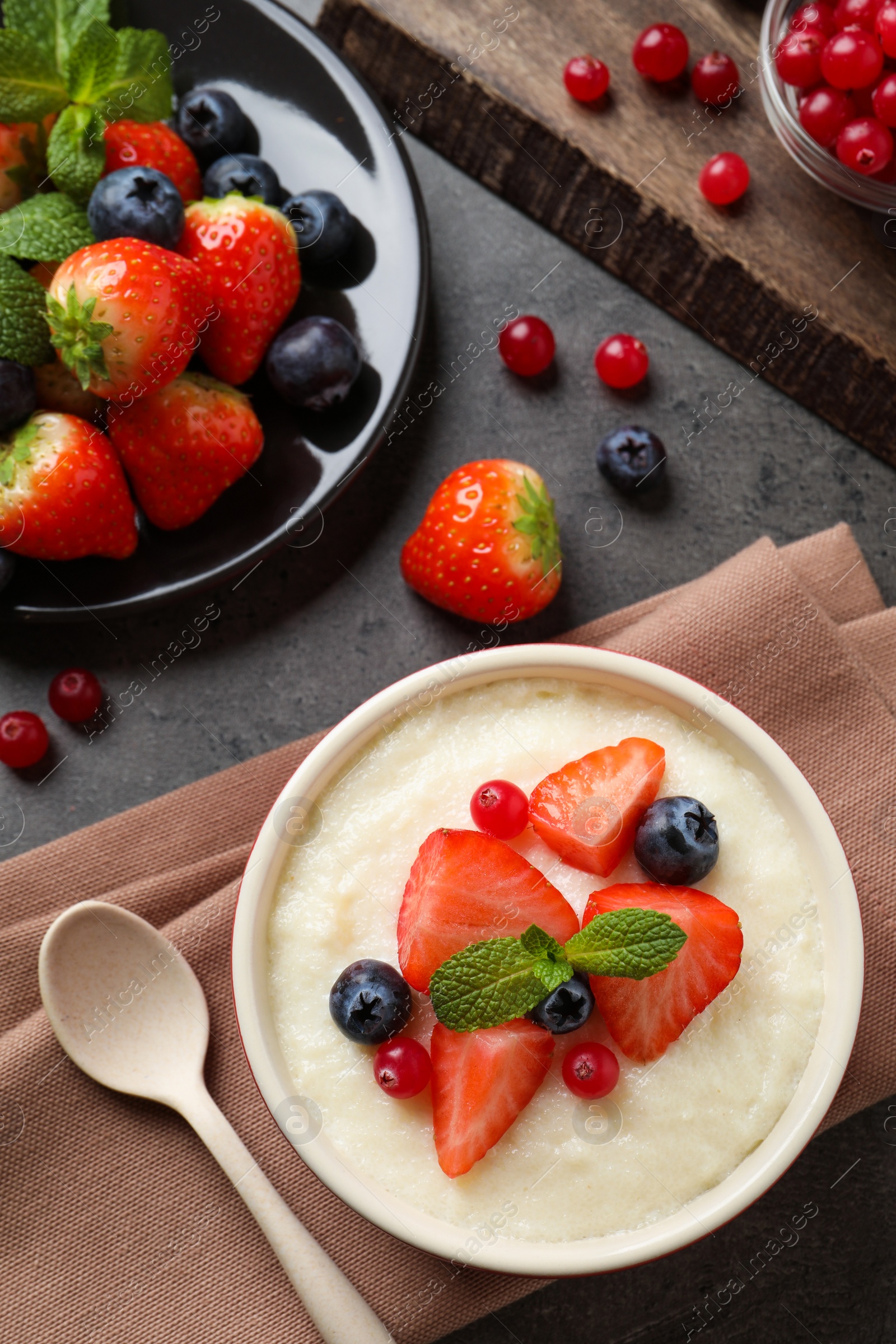 Photo of Delicious semolina pudding with berries and mint served on grey table, flat lay