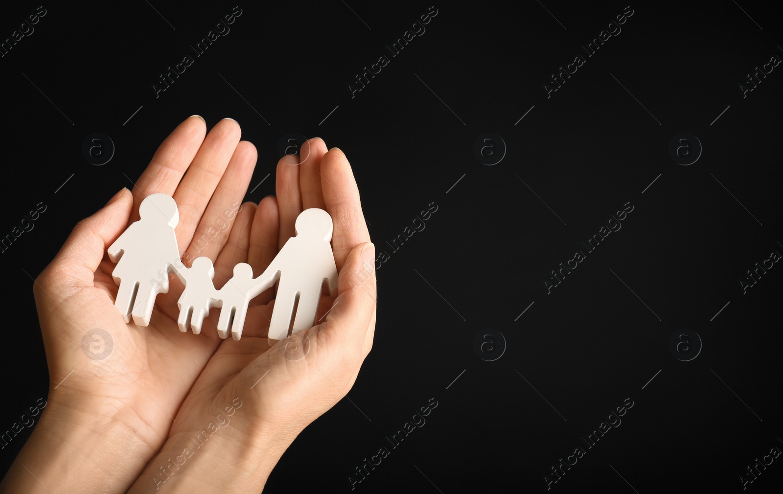 Photo of Woman holding figure of family in hands on black background, closeup. Space for text