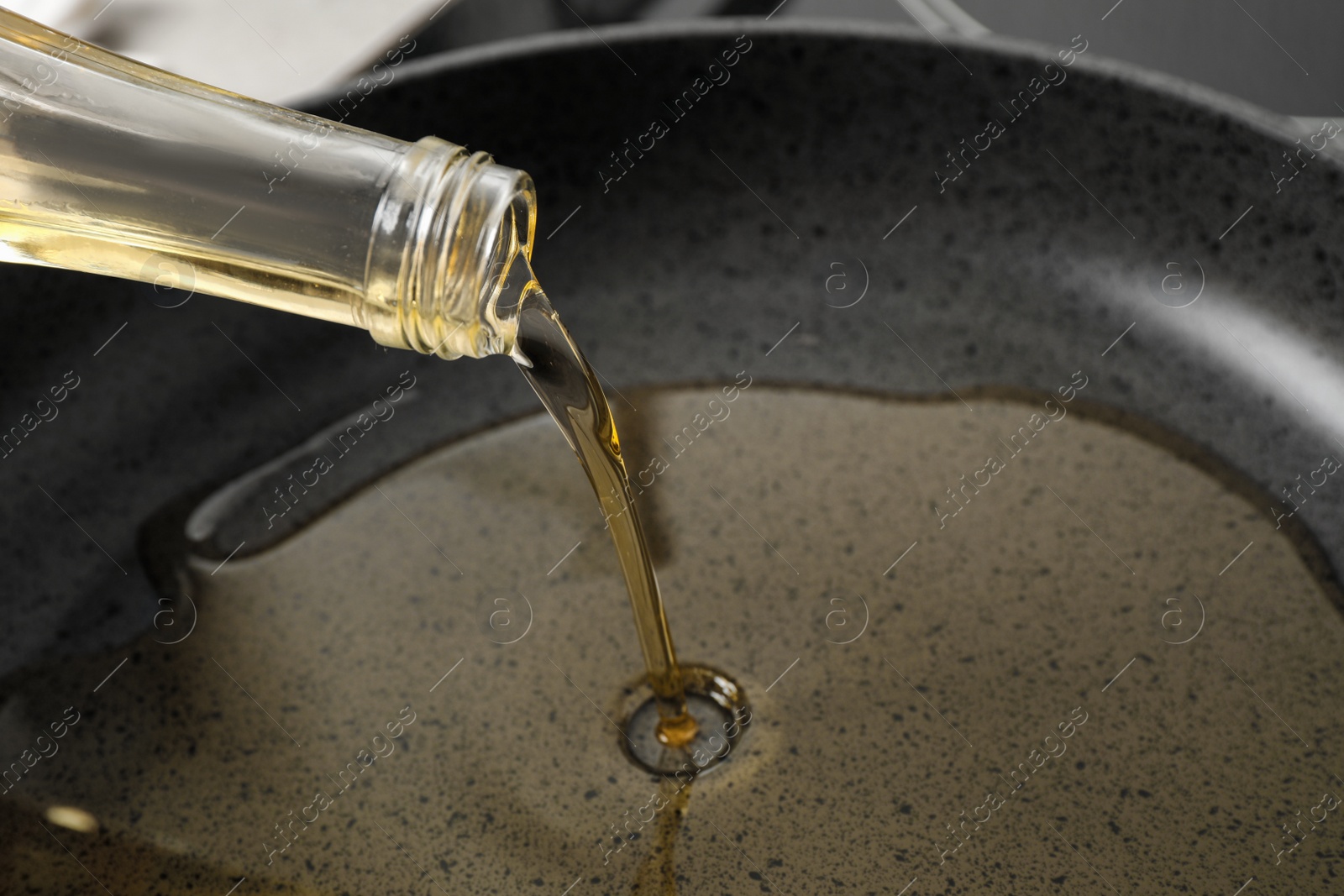 Photo of Pouring cooking oil from bottle into frying pan, closeup
