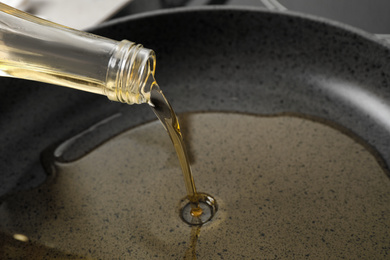 Photo of Pouring cooking oil from bottle into frying pan, closeup