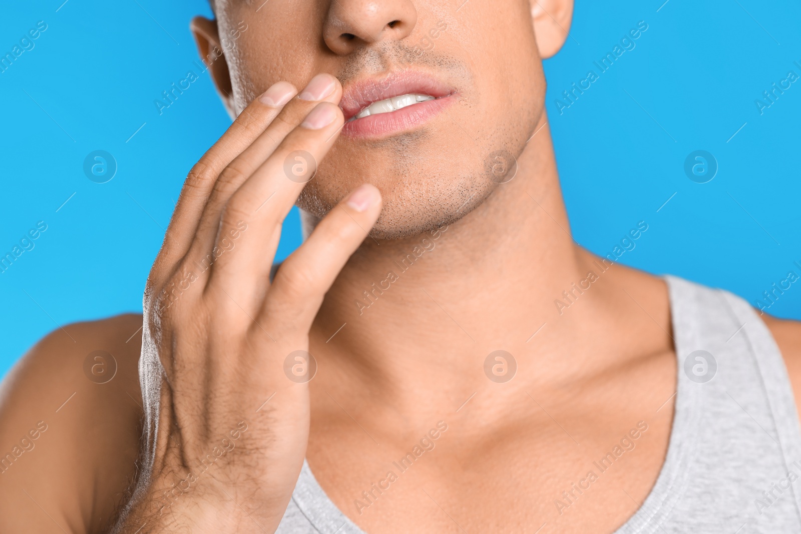 Photo of Man with herpes touching lips against light blue background, closeup