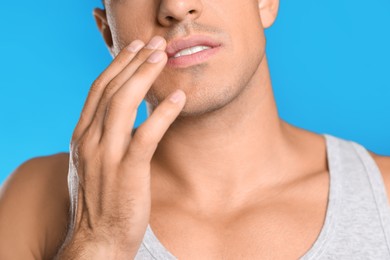 Photo of Man with herpes touching lips against light blue background, closeup