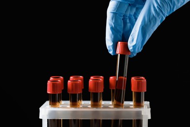 Photo of Scientist putting test tube with brown liquid into stand against black background, closeup