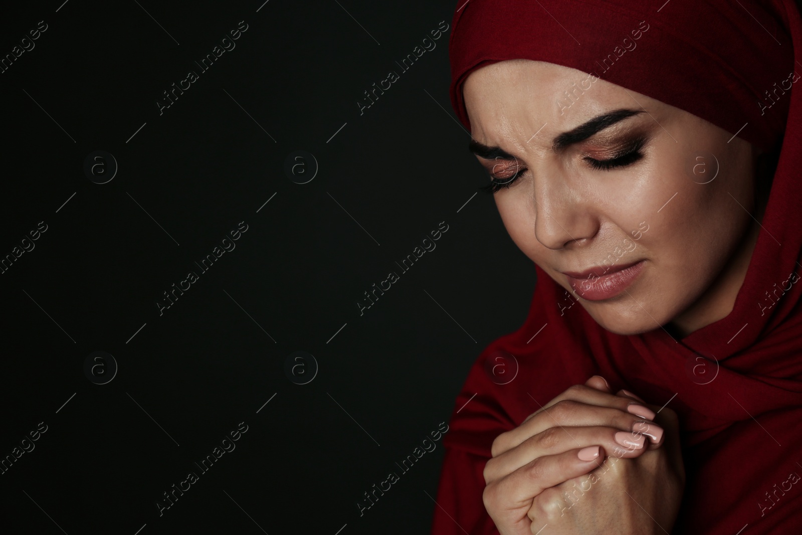 Photo of Portrait of sad Muslim woman in hijab  praying on dark background. Space for text