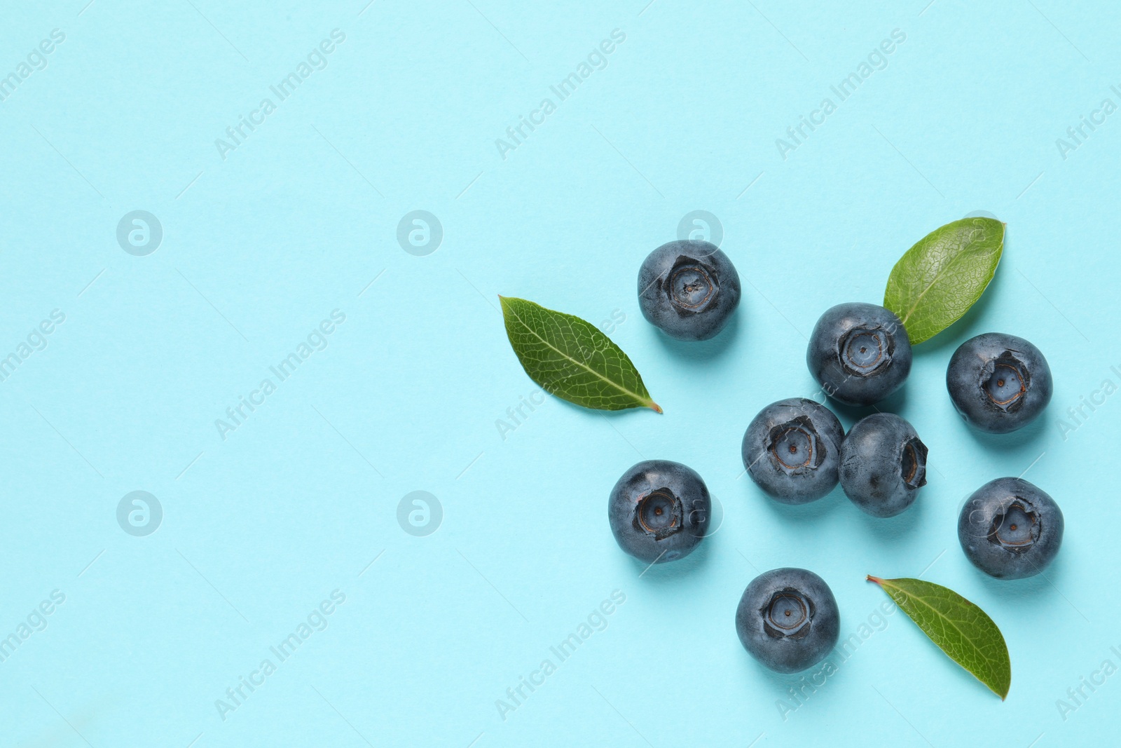 Photo of Tasty fresh blueberries with green leaves on light blue background, flat lay. Space for text