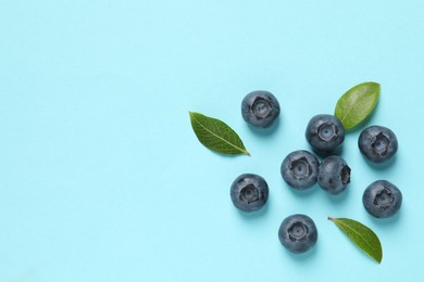 Tasty fresh blueberries with green leaves on light blue background, flat lay. Space for text