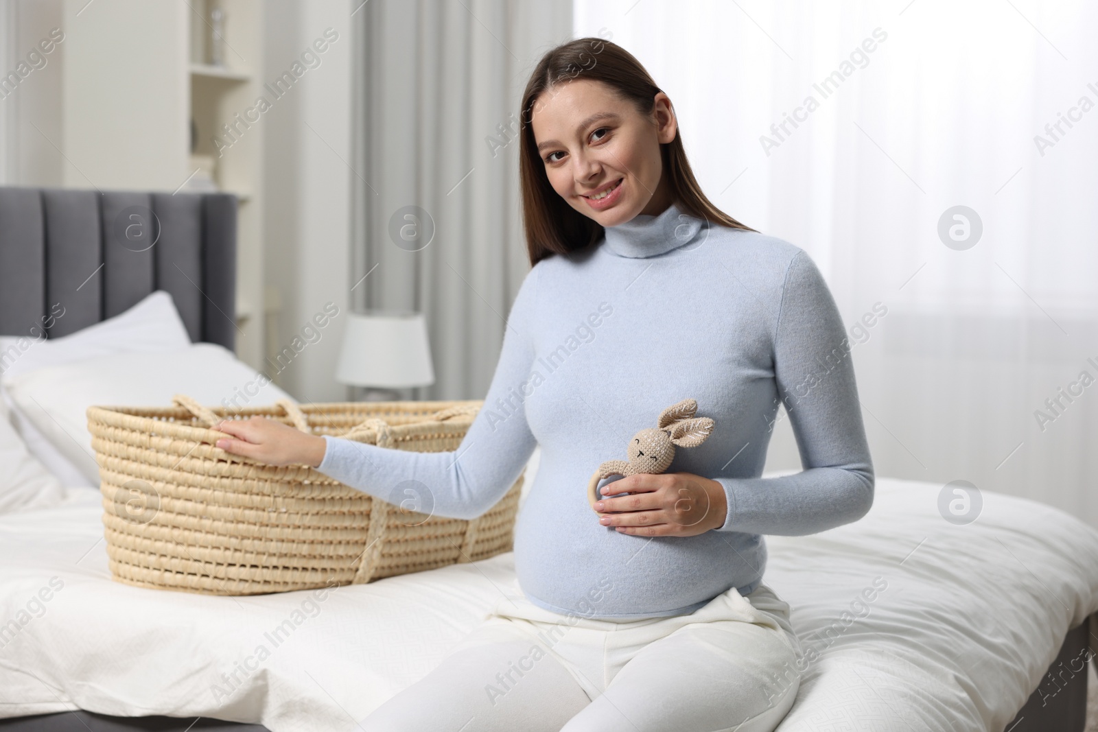 Photo of Beautiful pregnant woman with bunny toy and baby basket in bedroom