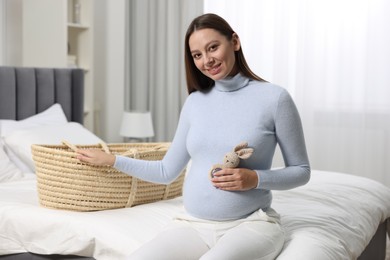 Beautiful pregnant woman with bunny toy and baby basket in bedroom