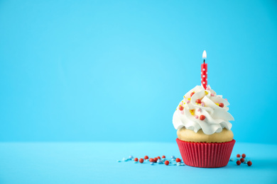 Photo of Delicious birthday cupcake with candle on light blue background. Space for text