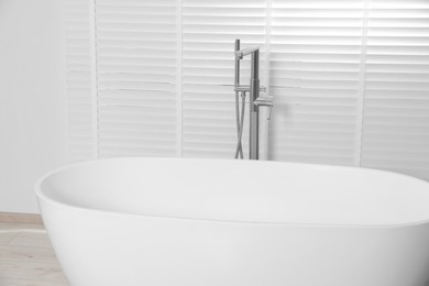 Stylish ceramic tub near window with blinds indoors