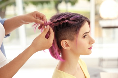 Photo of Professional stylist braiding woman's color hair in beauty salon. Modern trend
