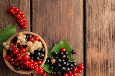 Photo of Different fresh ripe currants and green leaves on wooden table, flat lay. Space for text