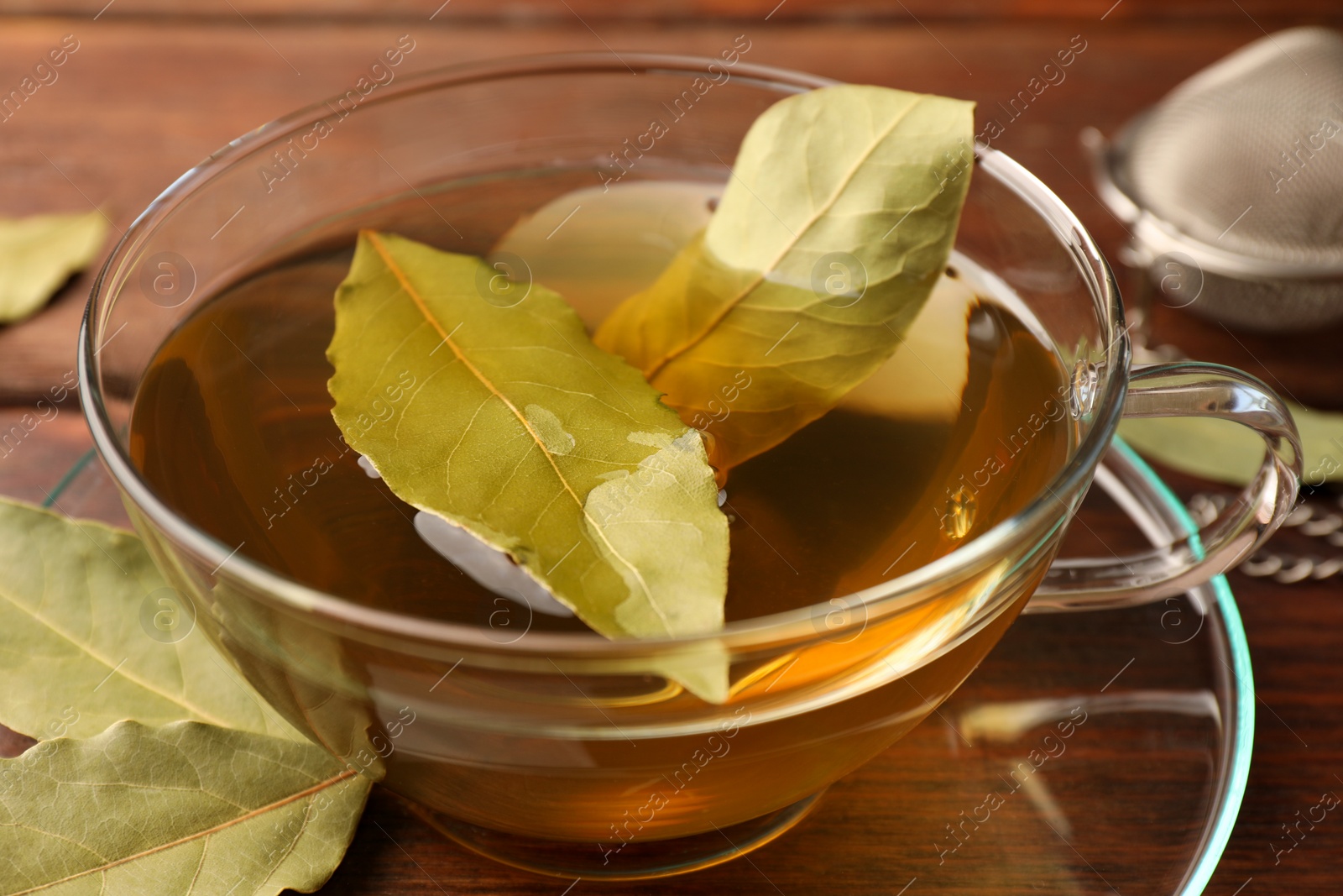 Photo of Cup of freshly brewed tea with bay leaves on wooden table, closeup