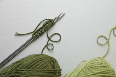 Photo of Soft green yarns, knitting and metal needles on light background, flat lay