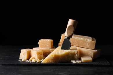 Photo of Parmesan cheese with slate plate and knife on black table
