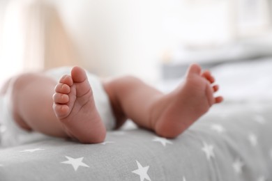 Photo of Cute little baby in diaper lying on bed in room, closeup