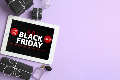 Photo of Tablet with Black Friday announcement, gifts and perfumes on violet background, flat lay. Space for text