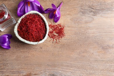 Photo of Dried saffron and crocus flowers on wooden table, flat lay. Space for text