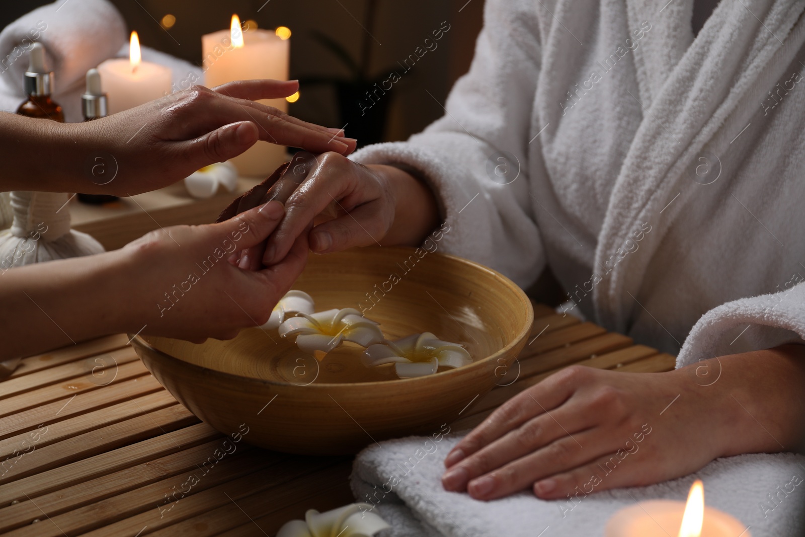 Photo of Woman receiving hand massage in spa salon, closeup. Bowl of water and flowers on wooden table