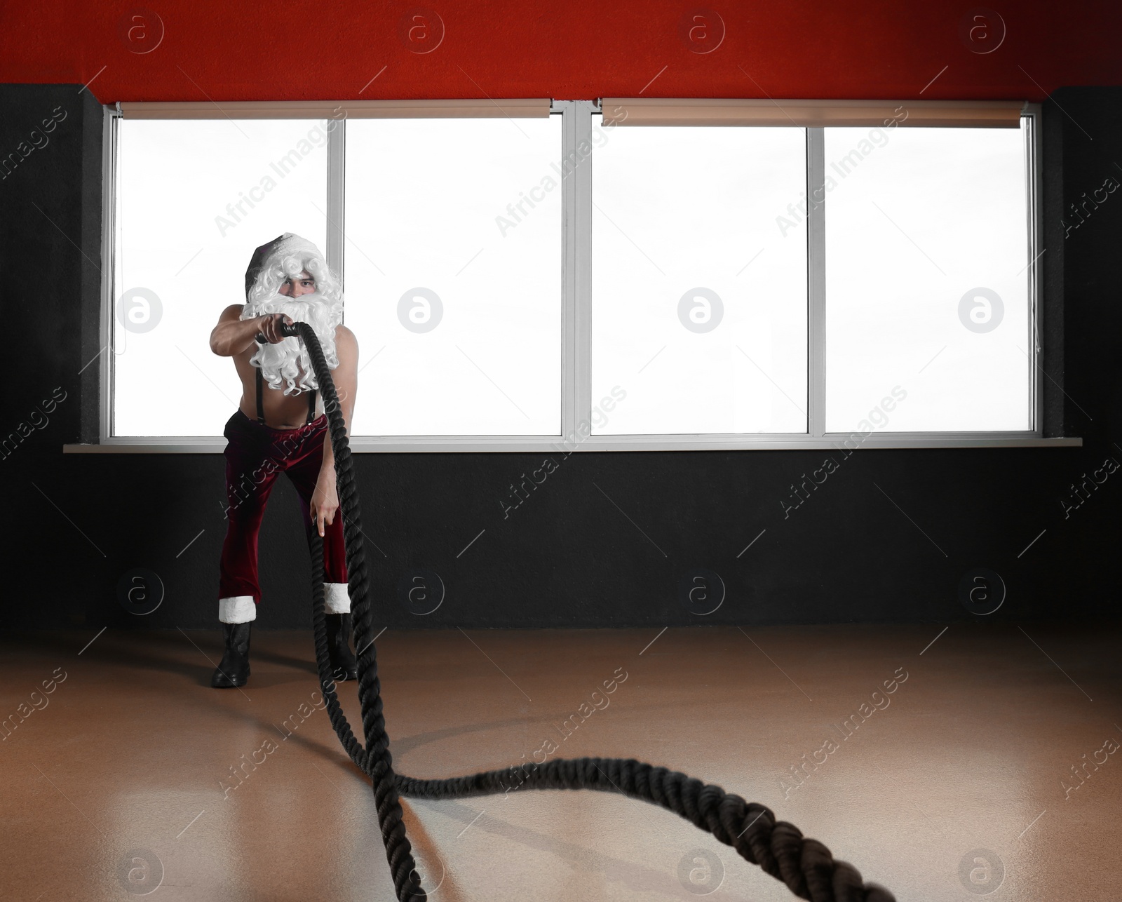 Photo of Young shirtless Santa Claus training with ropes in modern gym