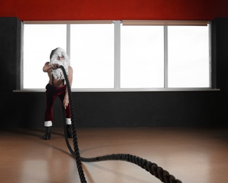 Young shirtless Santa Claus training with ropes in modern gym