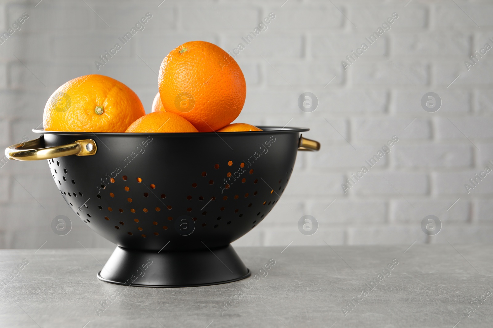 Photo of Fresh ripe oranges in black colander on light grey table. Space for text