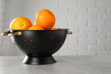 Photo of Fresh ripe oranges in black colander on light grey table. Space for text