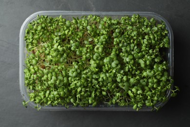 Photo of Sprouted arugula seeds in plastic container on grey table, top view