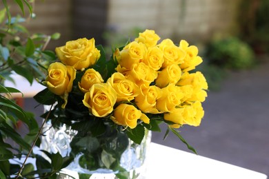 Beautiful bouquet of yellow roses in glass vase on white table outdoors