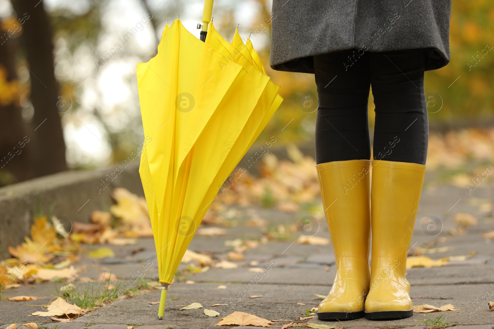 Photo of Woman with yellow umbrella and rubber boots in autumn park, closeup