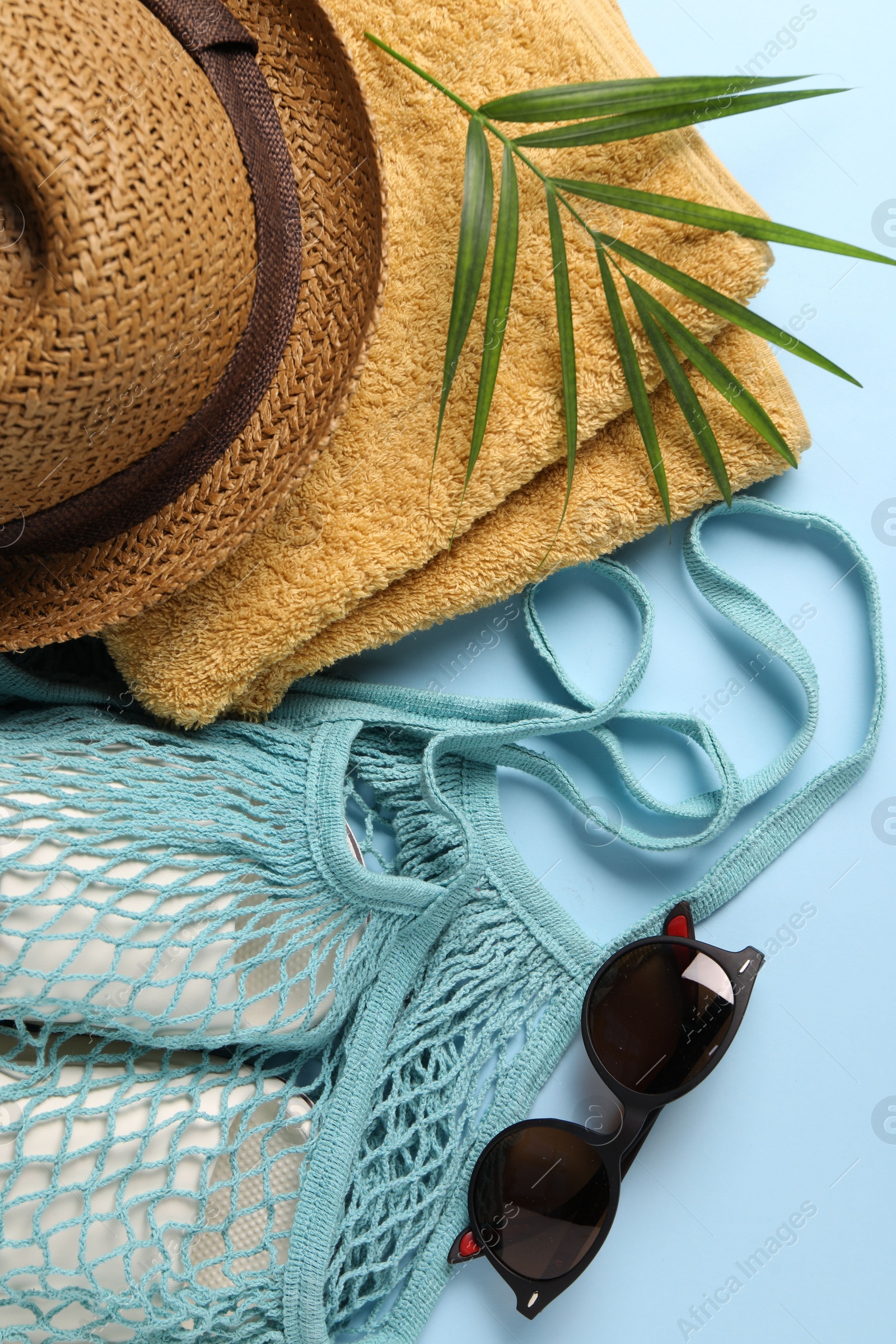 Photo of String bag, different beach accessories and palm leaf on light blue background, flat lay