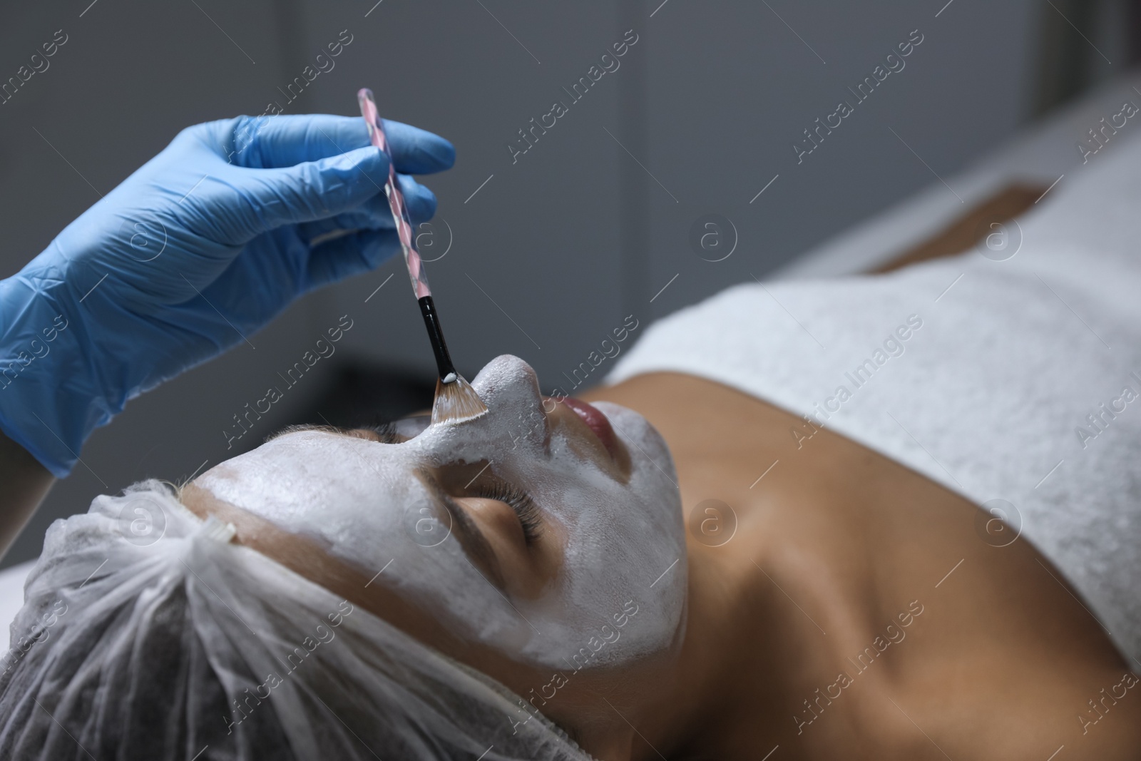 Photo of Cosmetologist applying mask on client's face in spa salon