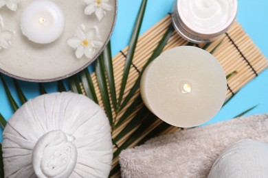 Photo of Flat lay composition with spa products, burning candle and beautiful flowers on light blue background