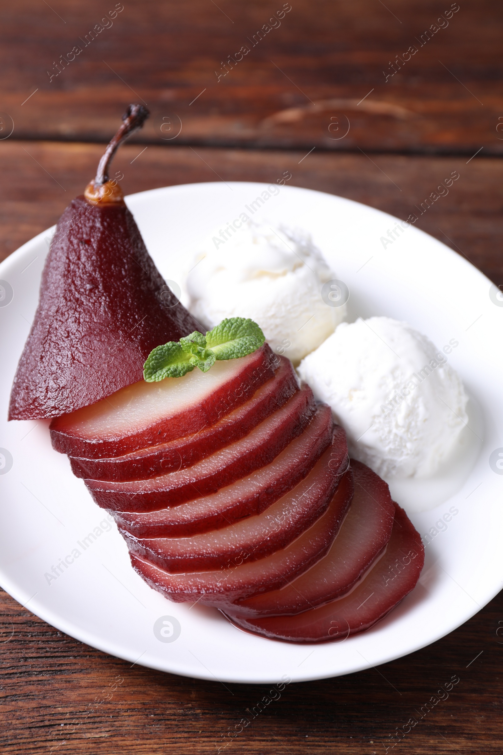 Photo of Tasty red wine poached pear and ice cream on wooden table, closeup