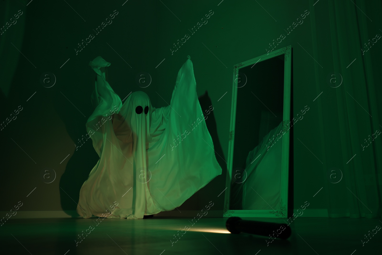 Photo of Creepy ghost. Woman covered with sheet near mirror in green light