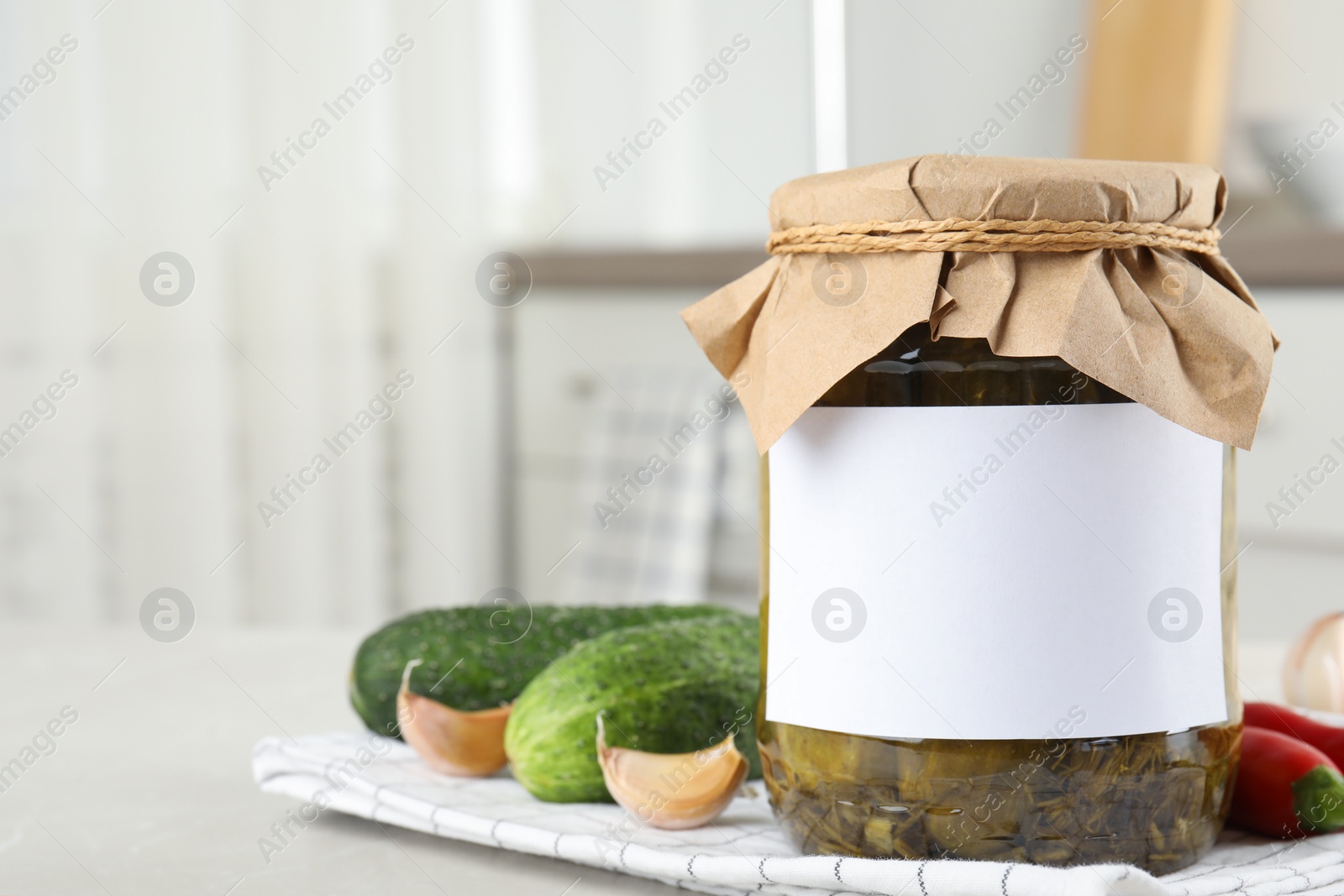 Photo of Jar of pickled cucumbers with blank sticker on grey table in kitchen, space for text