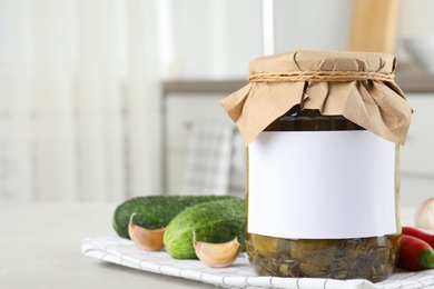 Photo of Jar of pickled cucumbers with blank sticker on grey table in kitchen, space for text