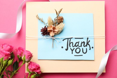 Photo of Card with phrase Thank You and beautiful flowers on pink background, flat lay