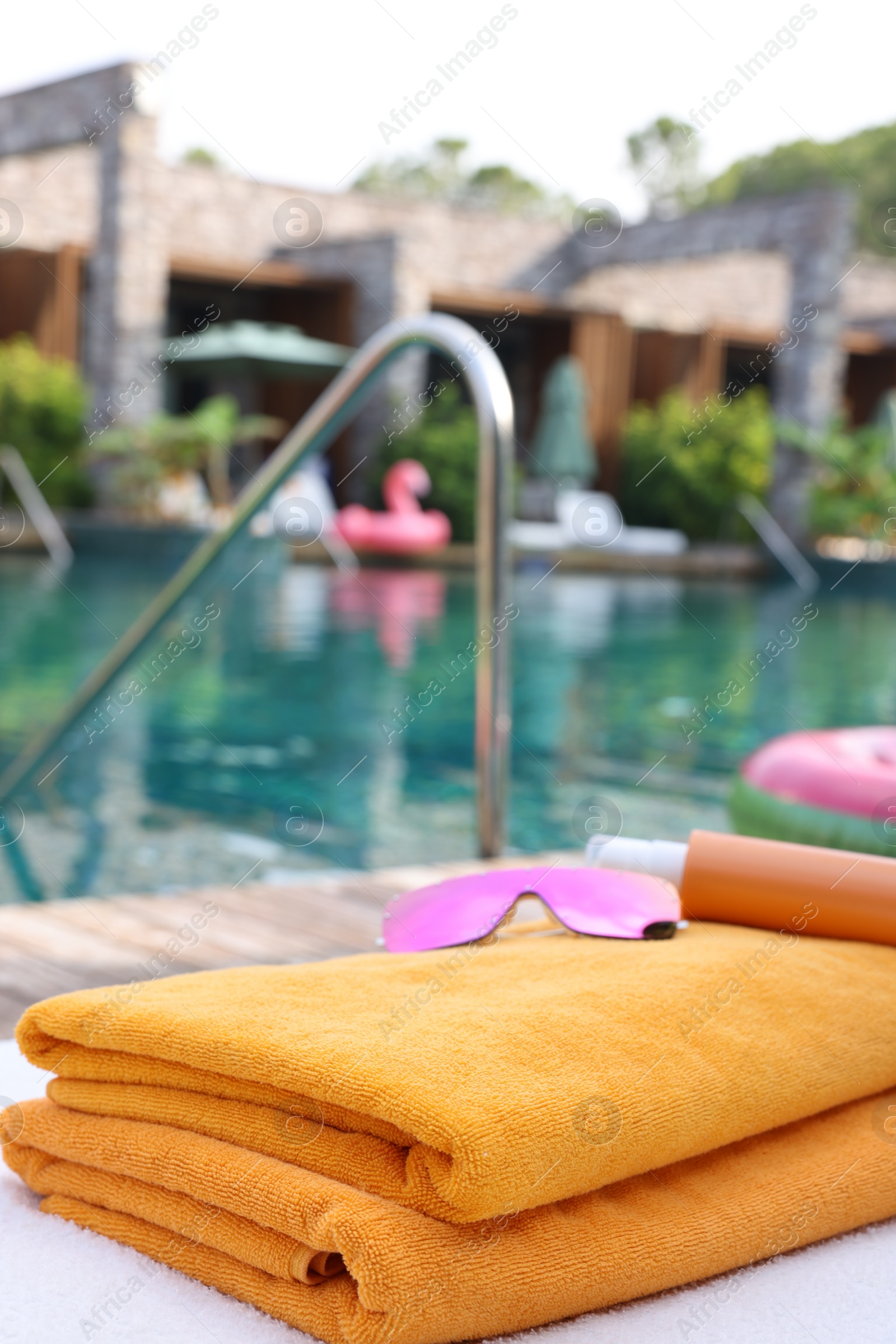 Photo of Beach towels, sunglasses and sunscreen on sun lounger near outdoor swimming pool, space for text. Luxury resort