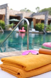 Beach towels, sunglasses and sunscreen on sun lounger near outdoor swimming pool, space for text. Luxury resort