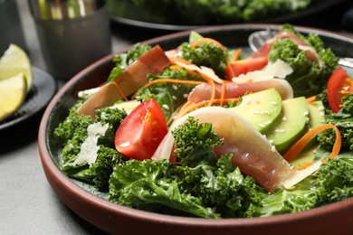 Photo of Delicious kale salad with prosciutto served on grey table, closeup