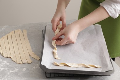Woman putting homemade breadsticks on baking sheet at light grey marble table, closeup. Cooking traditional grissini