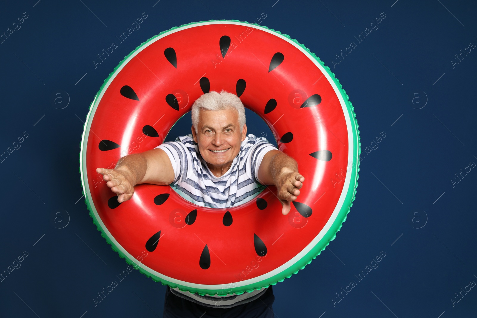 Photo of Funny mature man with bright inflatable ring on dark blue background